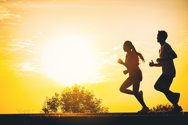 Silhouette eines jungen Paares, das zusammen auf der Straße mit Sonnenuntergangshintergrund läuft