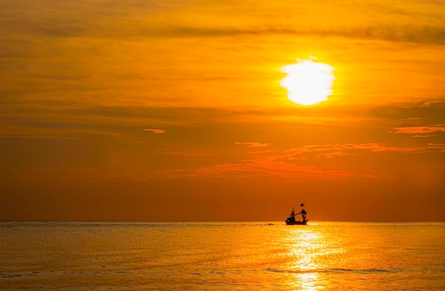 Silhouette eines kleinen Dorffischerboots, das morgens aufs Meer hinausfährt Das Meer hat morgens Wellen und Sonnenstrahlen