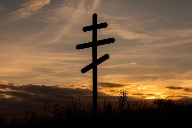 Foto silhouette eines kreuzes auf dem feld bei sonnenuntergang mit dramatischem himmel