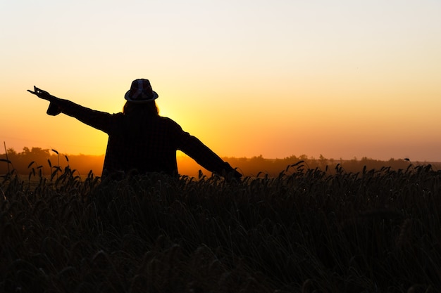 Silhouette eines Mädchens gegen die untergehende Sonne. junge Frau in einem Weizenfeld