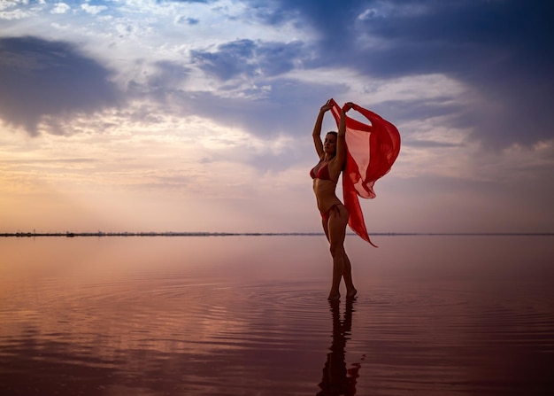 Silhouette eines Mädchens in einem roten Badeanzug am Strand Rotes Gewebe entwickelt sich in ihren Händen
