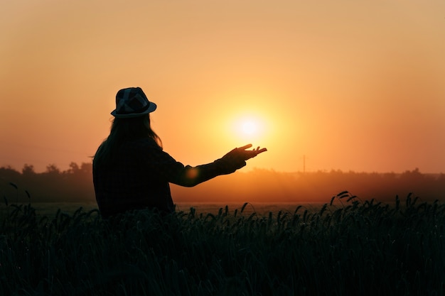 Silhouette eines Mädchens mit der untergehenden Sonne in ihren Händen. junge Frau mit der Sonne auf der Hand am Weizenfeld i