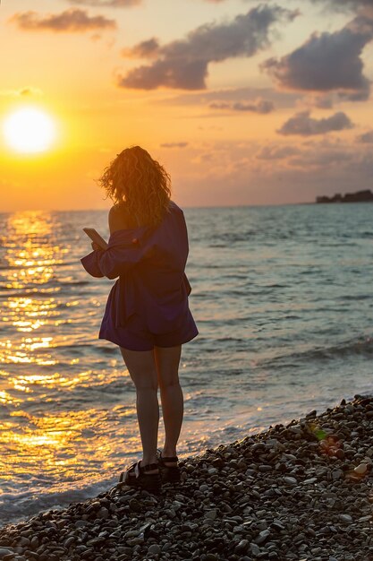 Silhouette eines Mädchens mit langen, gewellten Haaren mit einem Tablet am Abend am Meer