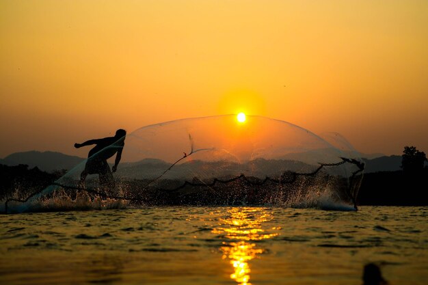 Foto silhouette eines mannes, der bei sonnenuntergang am see gegen den himmel angelt