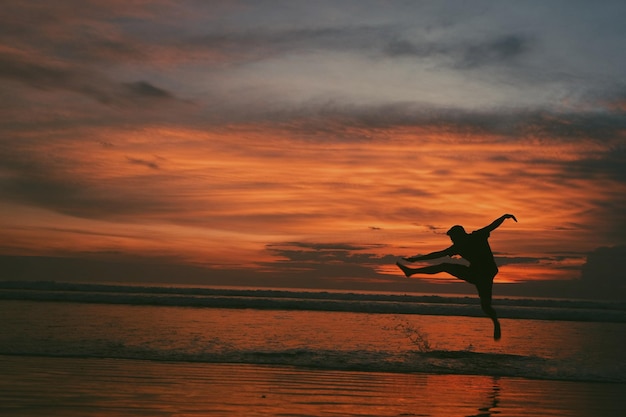 Silhouette eines Mannes, der bei Sonnenuntergang am Strand springt