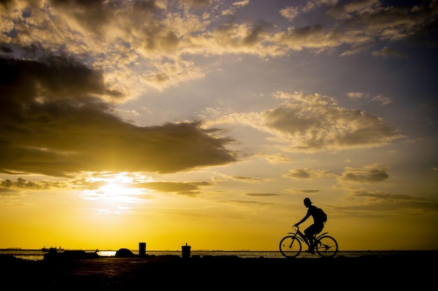 Silhouette eines Mannes, der bei Sonnenuntergang auf einem bewölkten Himmel durch das Meer fährt