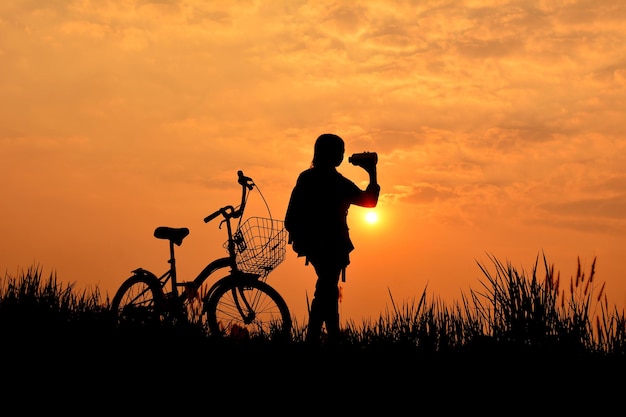 Silhouette eines Mannes, der bei Sonnenuntergang aus einer Flasche gegen den Himmel trinkt