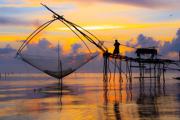 Foto silhouette eines mannes, der bei sonnenuntergang im meer gegen den himmel fischert