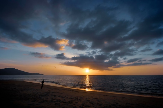 Silhouette eines Mannes, der den Sonnenuntergang am Meer mit ruhiger Atmosphäre am Strand auf der Insel Phuket Thailand betrachtet