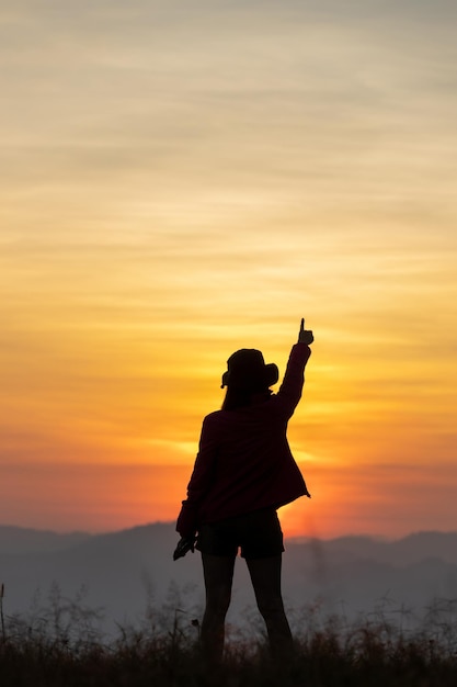 Silhouette eines Mannes, der die Hände auf dem Gipfel des Berges hält.