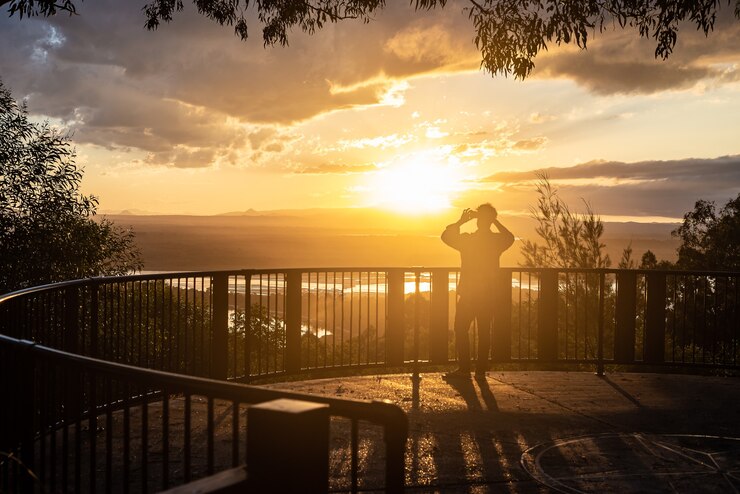Silhouette eines Mannes, der ein Foto mit Telefon in einem Lookout gegen einen bunten bewölkten Himmel bei Sonnenuntergang in Noosa, Queensland, Australien macht?