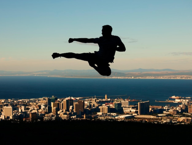 Silhouette eines Mannes, der Karate mit Himmel und Stadt im Hintergrund macht. Umriss eines männlichen Athleten, der in Kampfkunstbewegungen in die Luft schlägt und tritt Motivation, Inspiration und urbaner Krieger