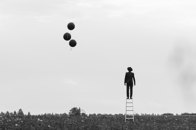 Silhouette eines Mannes in einem Anzug, der auf der Treppe in einem Feld mit Luftballons steht