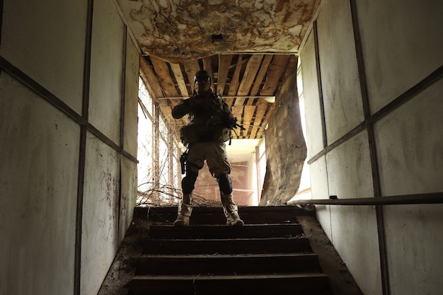 Silhouette eines Mannes in Uniform mit einer Waffe in einer alten Treppe in einem Glaskorridor in rotem Rauch