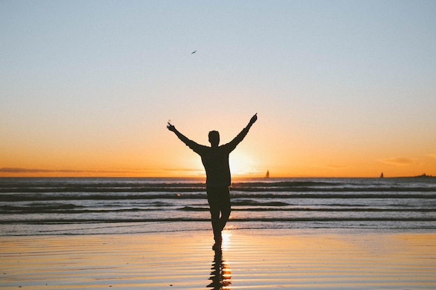 Foto silhouette eines mannes mit erhobenen armen, der bei sonnenuntergang am strand steht