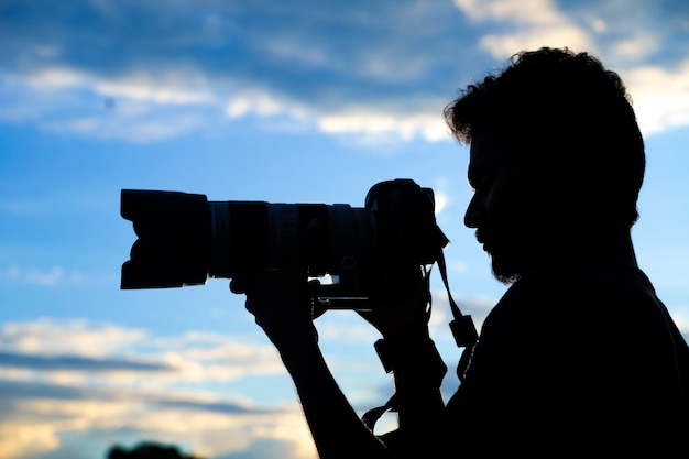 Silhouette eines mannfotografen mit dslr-kamera beim fotografieren bei sonnenuntergang