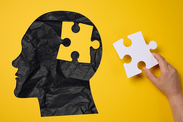 Silhouette eines menschlichen Kopfes, der ein Puzzlestück auf einem gelben Hintergrund hält, das die psychische Gesundheit darstellt