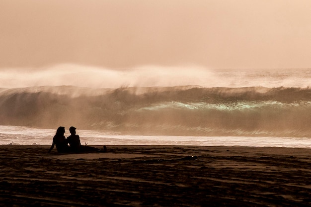 Silhouette eines Paares, das am Strand sitzt