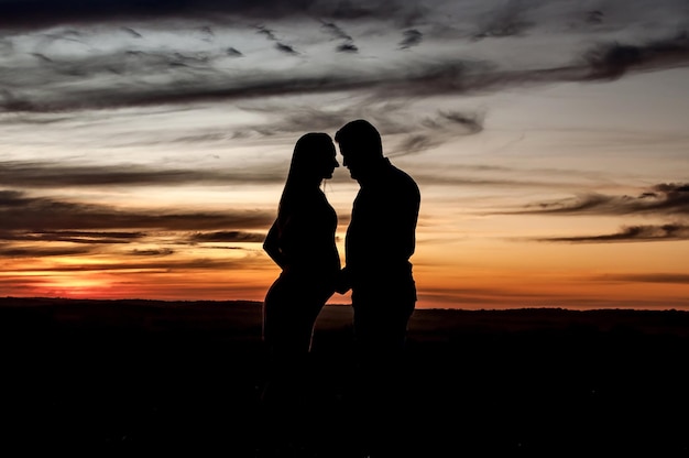Silhouette eines schwangeren verliebten Paares bei orangefarbenem Sonnenuntergang