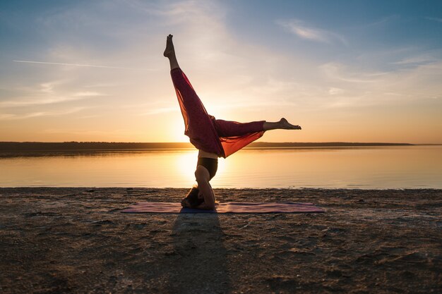 Silhouette Frau am Strand bei Sonnenuntergang Yoga Asana zu tun. Morgendliches Aufwärmtraining mit natürlicher Dehnung