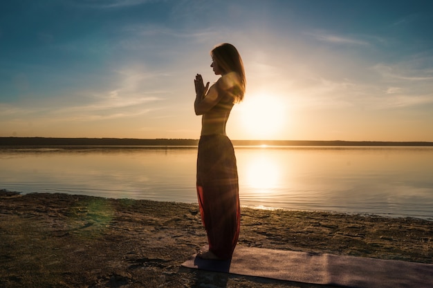 Silhouette Frau am Strand bei Sonnenuntergang Yoga Asana zu tun. Morgendliches Aufwärmtraining mit natürlicher Dehnung