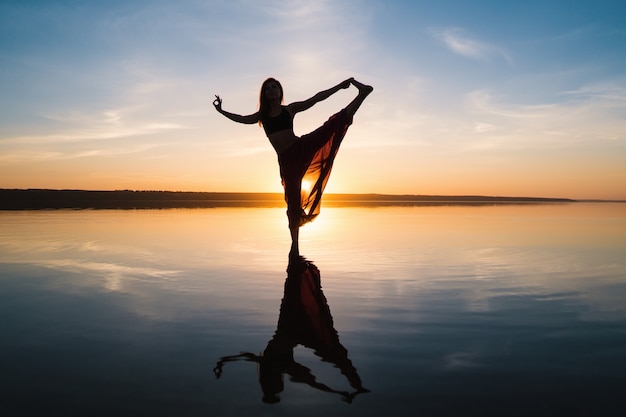 Silhouette Frau am Strand bei Sonnenuntergang Yoga Asana zu tun. Morgendliches Aufwärmtraining mit natürlicher Dehnung
