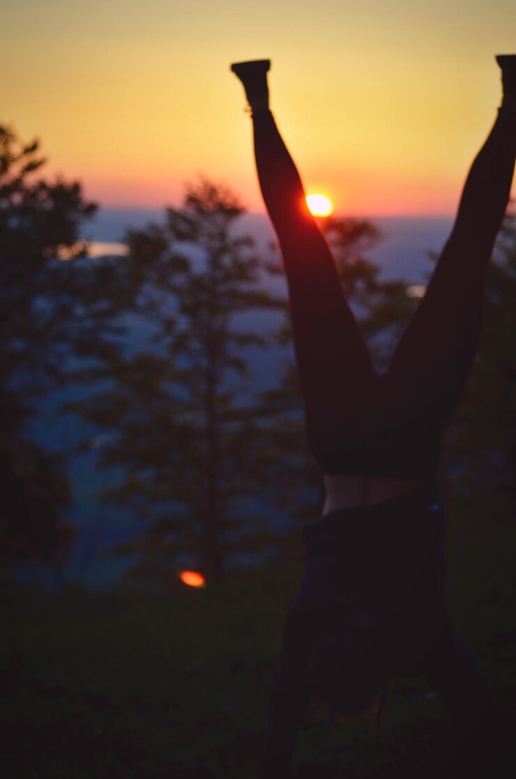 Foto silhouette frau macht handstand auf land gegen orangefarbenen himmel bei sonnenuntergang