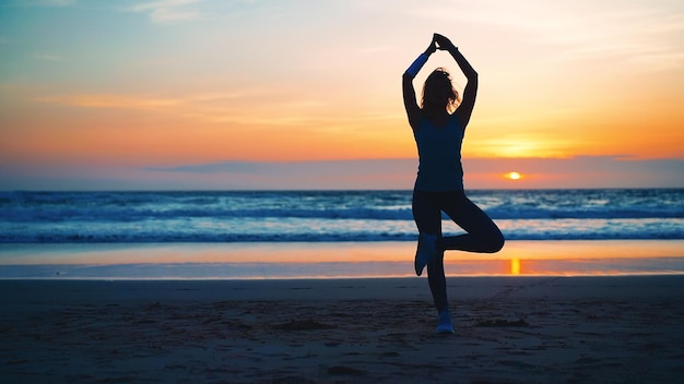 Silhouette Frau Yoga Baum Pose zur Meditation mit Sommerurlaub Strandglück und Entspannung Ruhige weibliche Übung mit Yoga meditieren Ozeanstrand mit Sonnenuntergang goldene Zeit