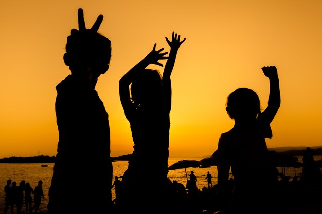 Foto silhouette freunde stehen am strand gegen orangefarbenen himmel bei sonnenuntergang