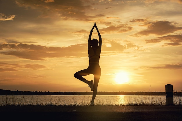 Silhouette junge Frau praktiziert Meditation Yoga am Strand bei Sonnenuntergang