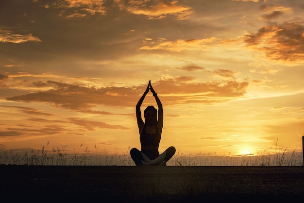 Silhouette junge Frau praktiziert Meditation Yoga am Strand bei Sonnenuntergang