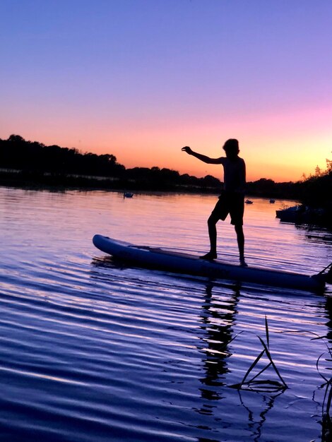 Foto silhouette-junge steht bei sonnenuntergang auf einem paddleboard