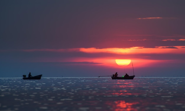 Silhouette kleines Fischerboot im Meer mit Sonnenuntergang bei schwacher Beleuchtung in der Dämmerung.