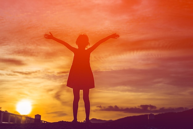 Silhouette Mädchen mit ausgestreckten Armen steht gegen den orangefarbenen Himmel
