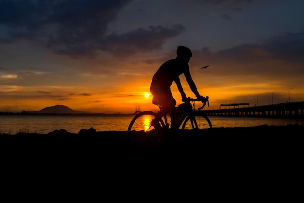 Silhouette Mann fährt Fahrrad am Strand gegen den Himmel während des Sonnenuntergangs