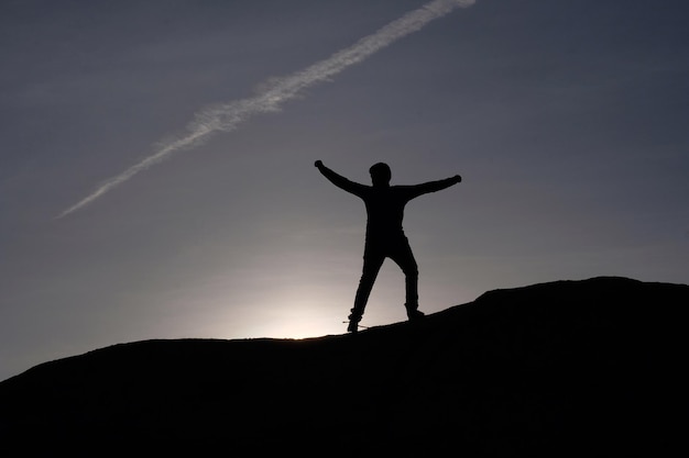 Silhouette Mann mit ausgestreckten Armen steht auf dem Berg gegen den Himmel