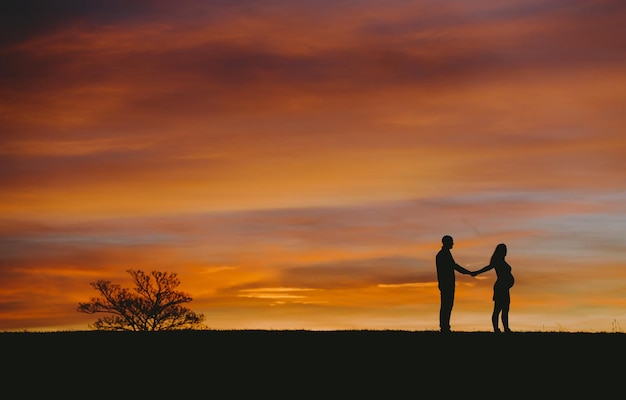 Silhouette Mann mit schwangerer Frau steht auf dem Feld gegen den Himmel bei Sonnenuntergang