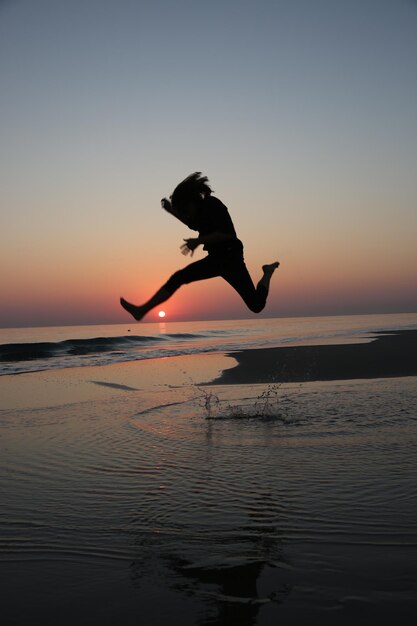 Foto silhouette mann springt am strand gegen den himmel bei sonnenuntergang