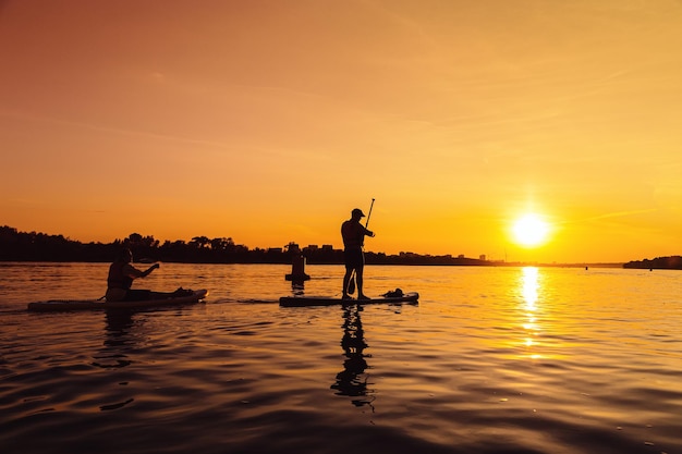 Silhouette Mann stehend auf sapboard Man fährt mit dem Boot auf dem Fluss bei Sonnenuntergang mit schöner Aussicht