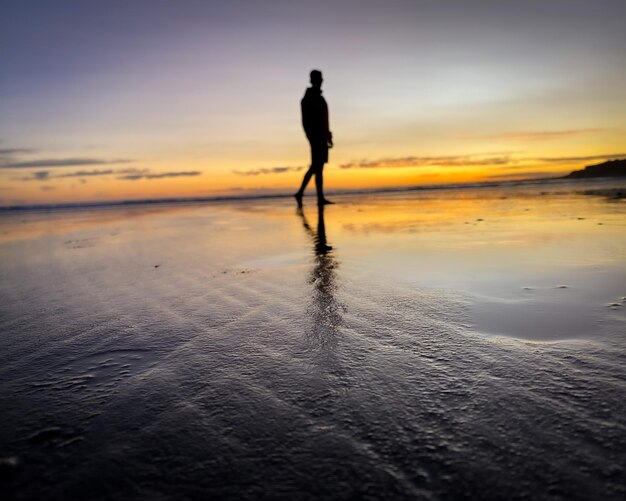 Foto silhouette mann steht am strand gegen den himmel während des sonnenuntergangs