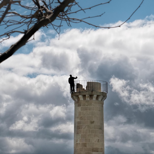 Foto silhouette mann steht auf dem turm und macht ein selfie gegen den bewölkten himmel