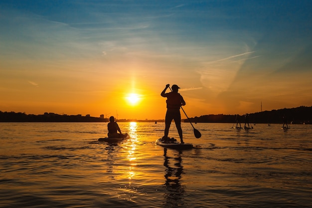 Silhouette Mann steht auf Sapboard Mann fährt Boot auf dem Fluss bei Sonnenuntergang mit schöner Aussicht