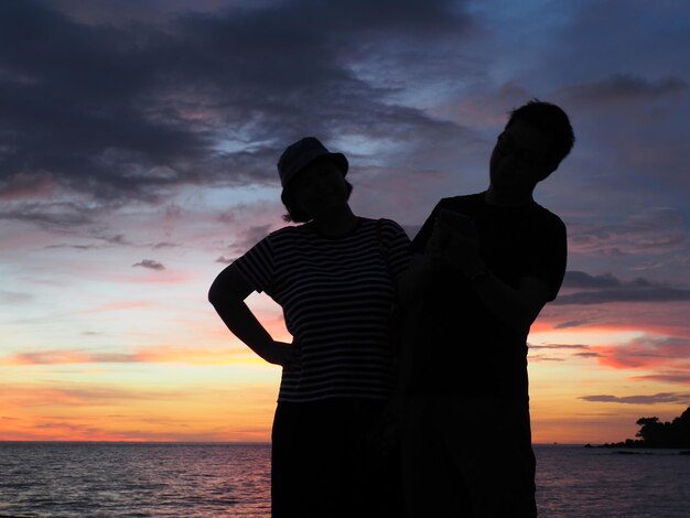 Silhouette Mann und Frau stehen am Meer gegen den Himmel während des Sonnenuntergangs