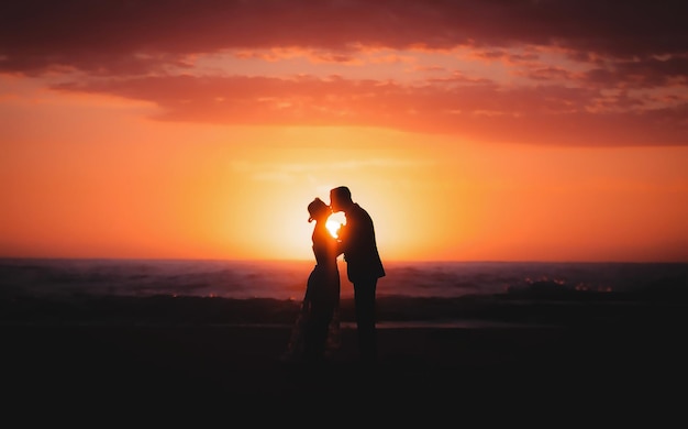 Silhouette-Paar küsst sich auf einer Klippe und steht gegen den orangefarbenen Sonnenuntergang