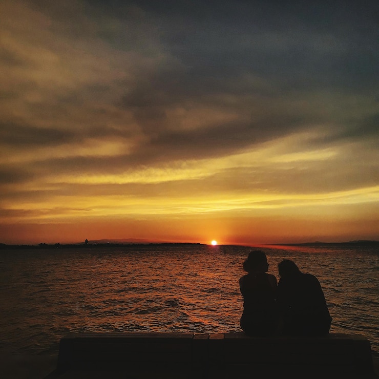 Foto silhouette-paar sitzt auf einem sitz am meer gegen einen orangefarbenen himmel