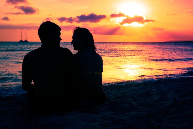 Silhouette-Paar sitzt beim Sonnenuntergang am Strand gegen den Himmel