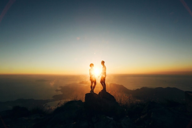 Silhouette-Paar steht bei Sonnenuntergang auf einer Felsformation gegen den Himmel