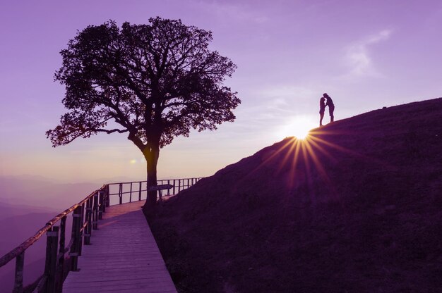 Silhouette-Paar steht während des Sonnenuntergangs auf dem Berg gegen den Himmel