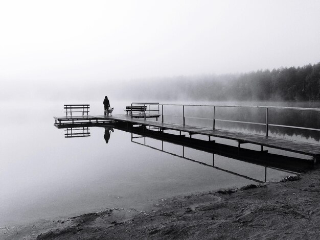 Silhouette Person mit Hund am Pier über dem See bei nebligem Wetter