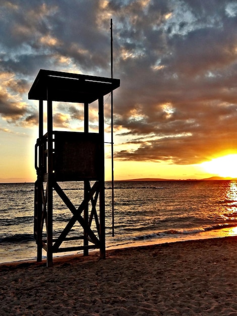 Silhouette Rettungsschwimmerhütte am Strand gegen bewölkten Himmel bei Sonnenuntergang